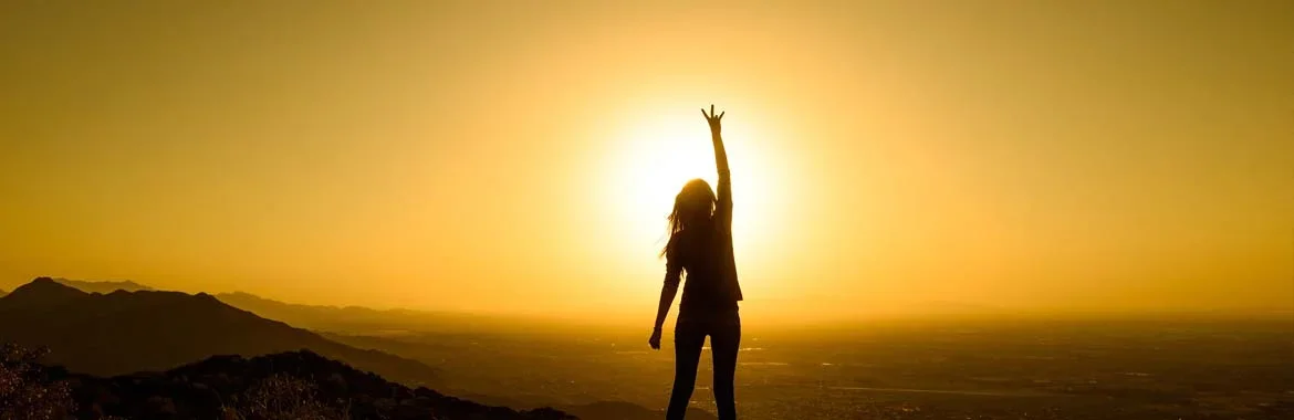 person in front of sunset with pitchfork hand sign